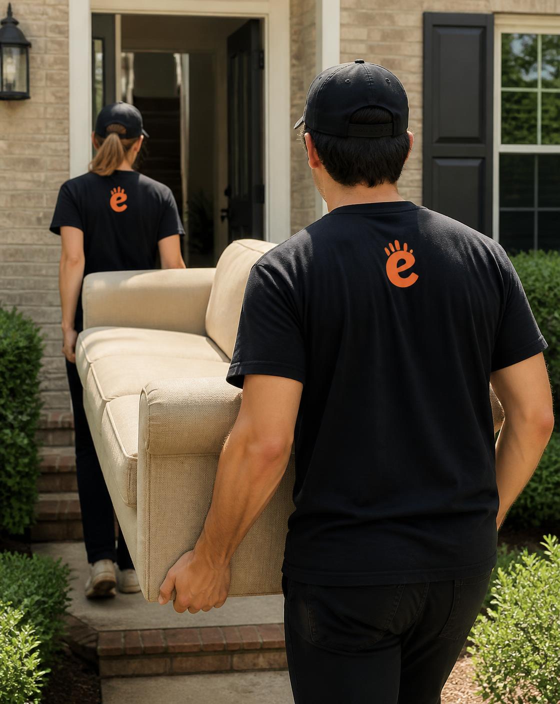 Two ExtraHands helpers in branded black uniform t-shirts carrying a sofa up to a Houston home's front door